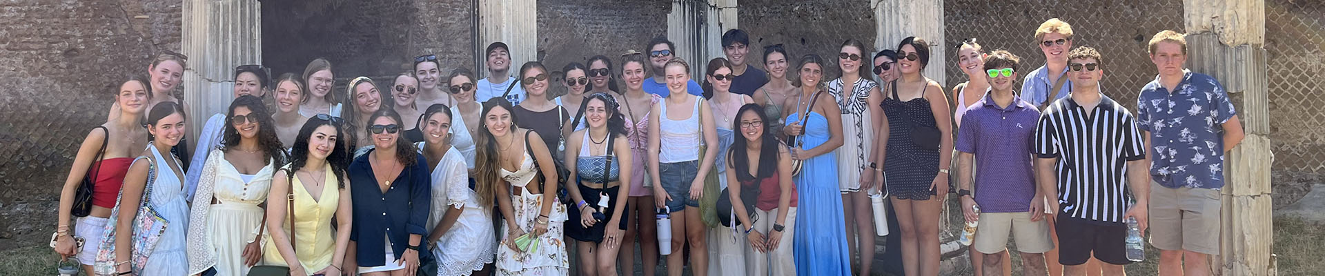 A large group of people posing together for a group photo in front of ancient stone columns and ruins